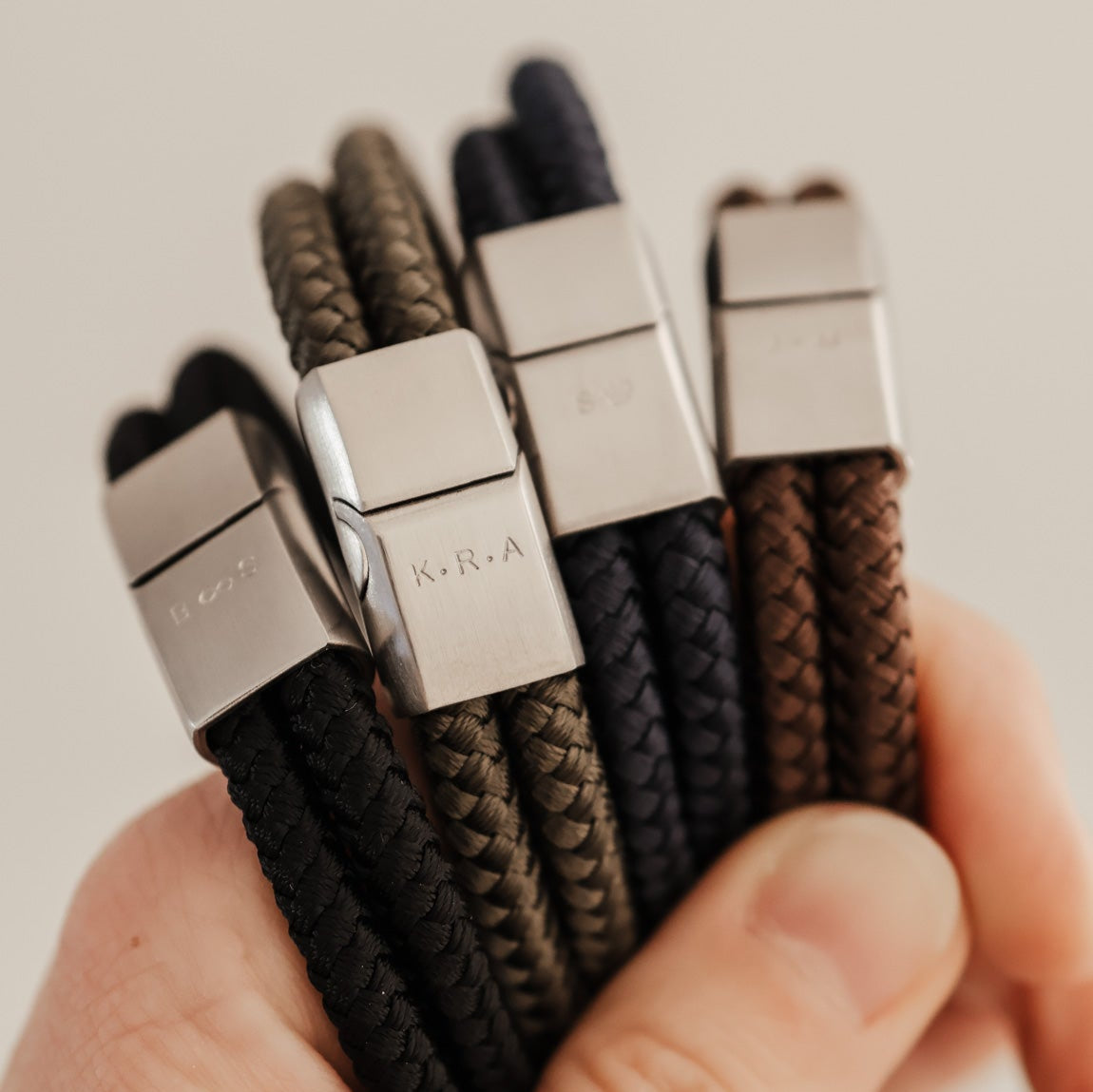 Hand holding three woven bracelets with metal clasps against a neutral background
