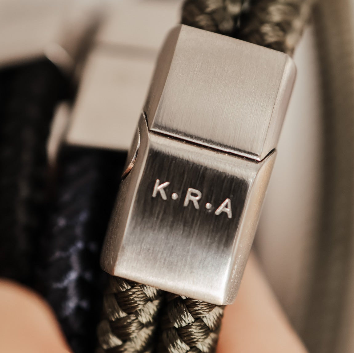 Close-up of a bracelet with a metal clasp engraved with 'K.R.A.'