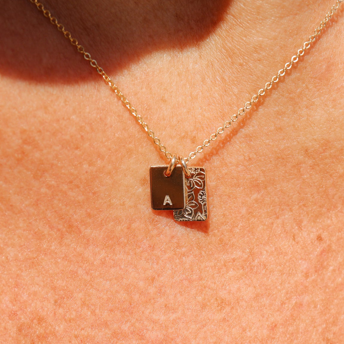 Gold necklace with a square pendant featuring an 'A' on a person's neck.