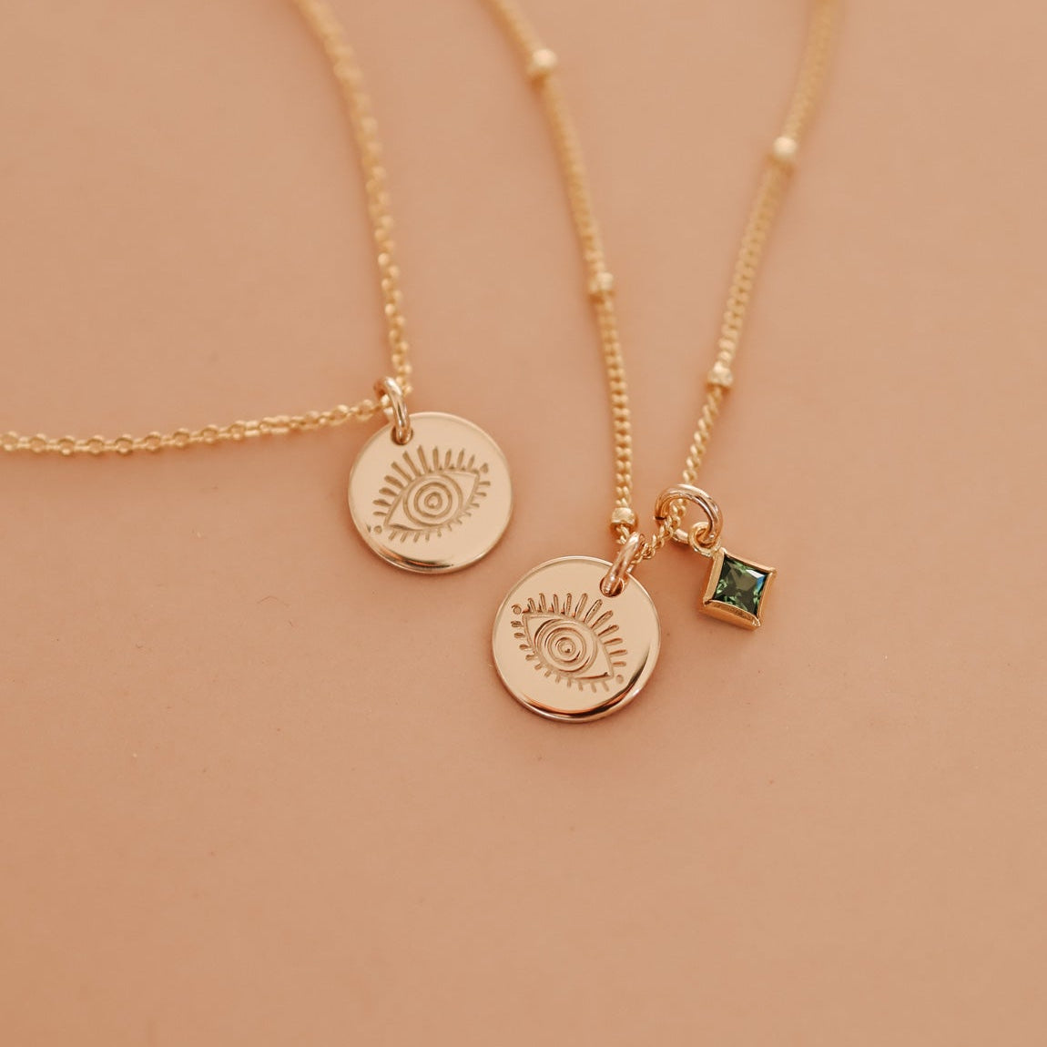 Two delicate gold satelite chain necklaces with small evil eye pendants and a small square green birthstone accent. Brisbane personalised jewellery