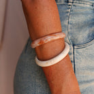 Close-up of a person's arm wearing two shell bracelets with a blurred background. - KBN RESIN BANGLES
